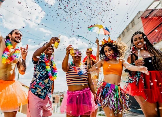 Foto colorida de grupo de foliões em Carnaval brindando - Metrópoles