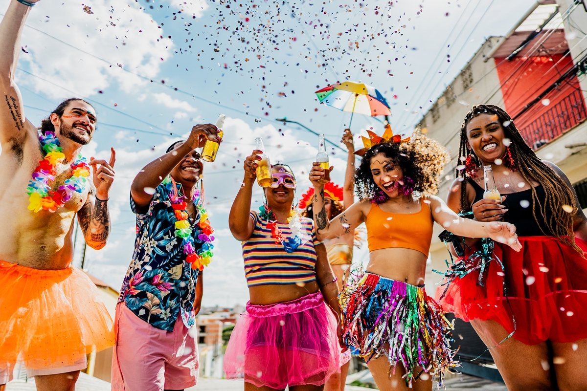 Foto colorida de grupo de foliões em Carnaval brindando - Metrópoles