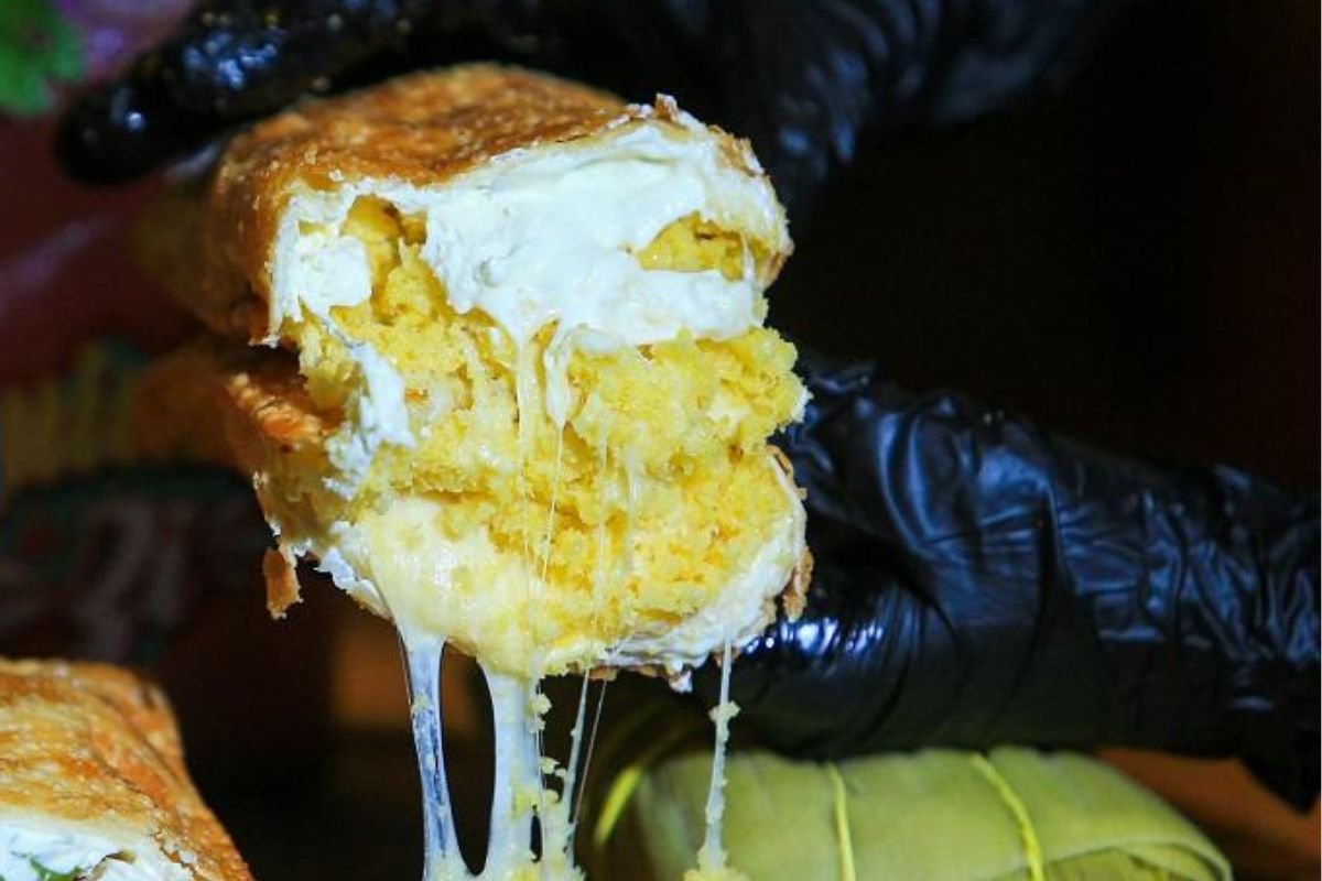 mão de luva segurando pastel de pamonha